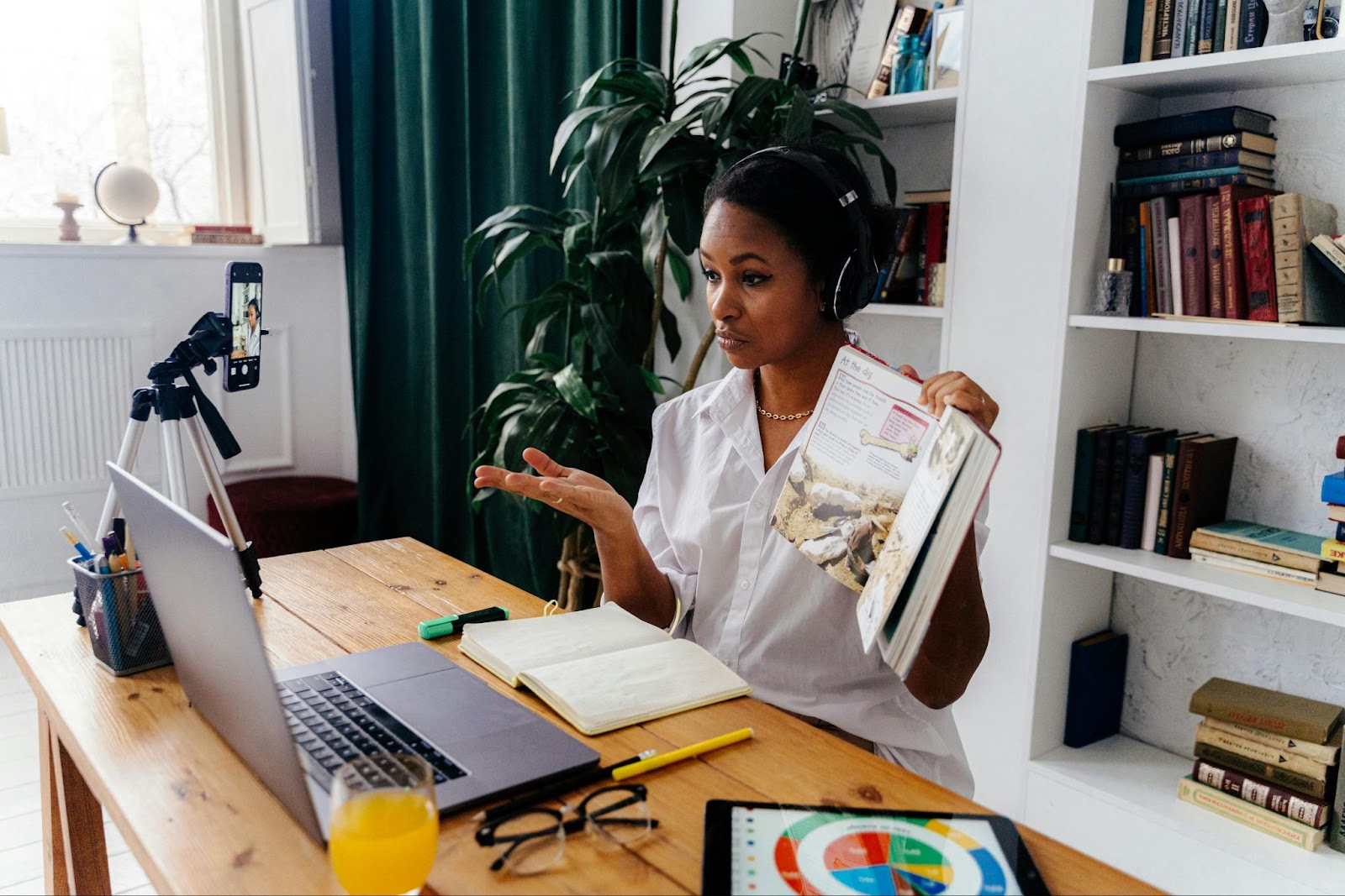 Woman filming an educational explainer video at home using a smartphone and laptop setup.