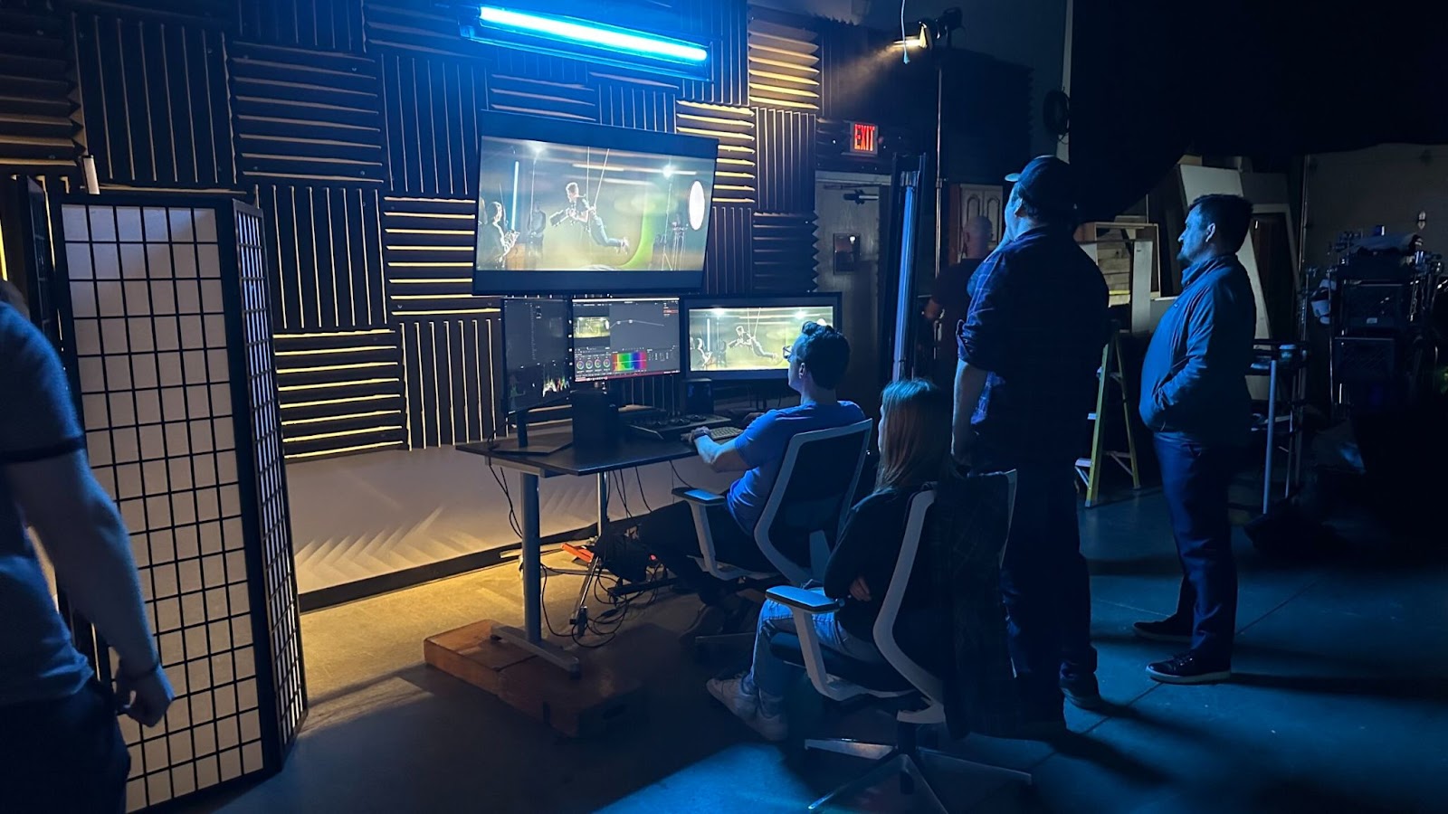 Marketing team in a dark studio reviewing video content on multiple screens during the editing phase of a video marketing strategy campaign.