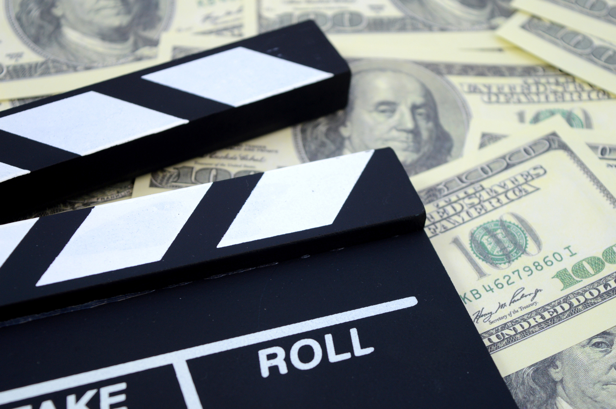 Film clapperboard on dollar bills representing video production costs and budget planning
