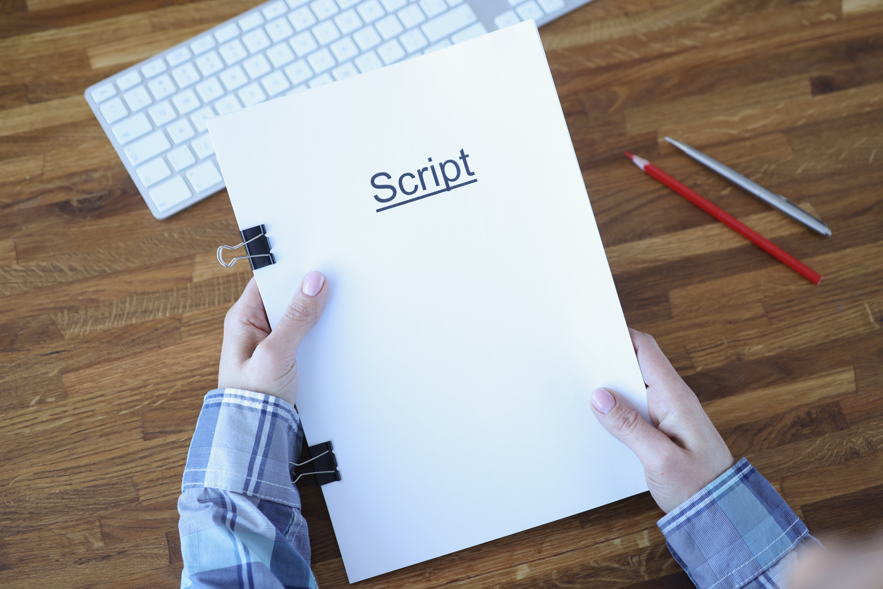Person holding explainer video script document with keyboard and writing tools on wooden desk