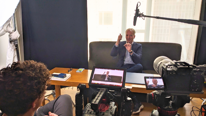 4 | Backflip Creative Marketing Corporate interview shoot in a bright office setting, featuring a business executive speaking on camera while the video crew films with cinema-grade gear and directional audio setup.