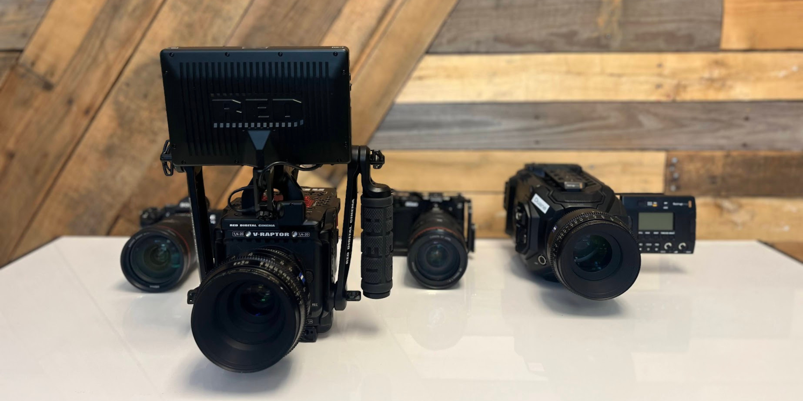 Four professional cinematic cameras with various lenses sit atop a white countertop in front of a wood background.